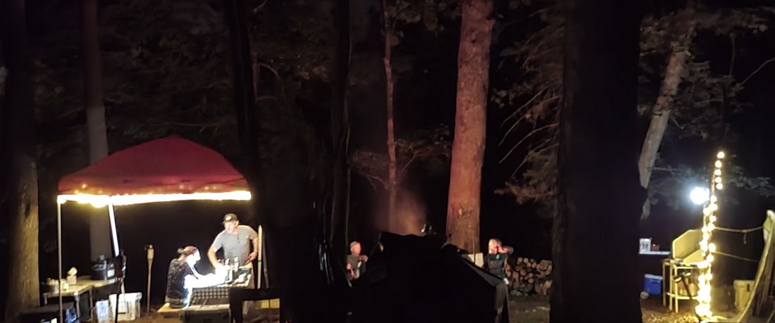 A camp canopy lit by string lights among dark trees at night