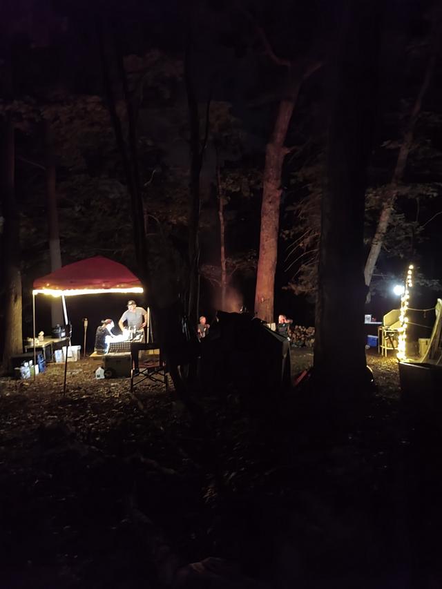A camp canopy lit by string lights among dark trees at night