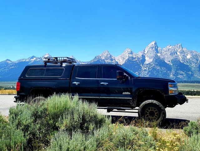 The black overland truck in profile, the Teton range rising behind it
